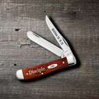 Case Religious Sayings Disciple Chestnut Bone Mini Trapper pocket knife with Clip and Spey blades open on a rustic wood surface, Matthew 28:19-20 on the Clip blade and Disciple script on the smooth chestnut bone handle