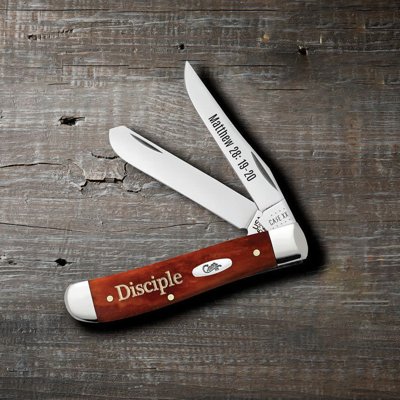 Case Religious Sayings Disciple Chestnut Bone Mini Trapper pocket knife with Clip and Spey blades open on a rustic wood surface, Matthew 28:19-20 on the Clip blade and Disciple script on the smooth chestnut bone handle