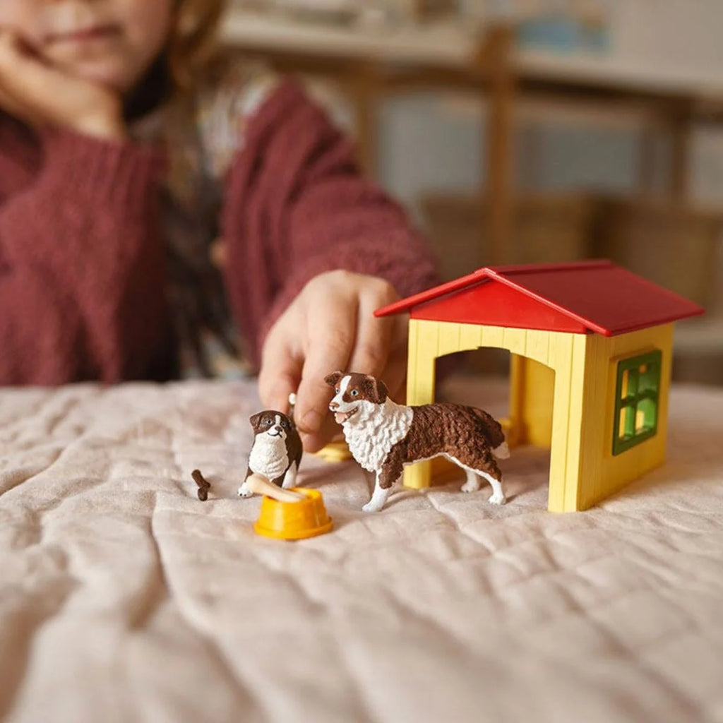 Child playing with Schleich Friendly Dog House, adult dog and puppy figures, bowl, bone and stick.