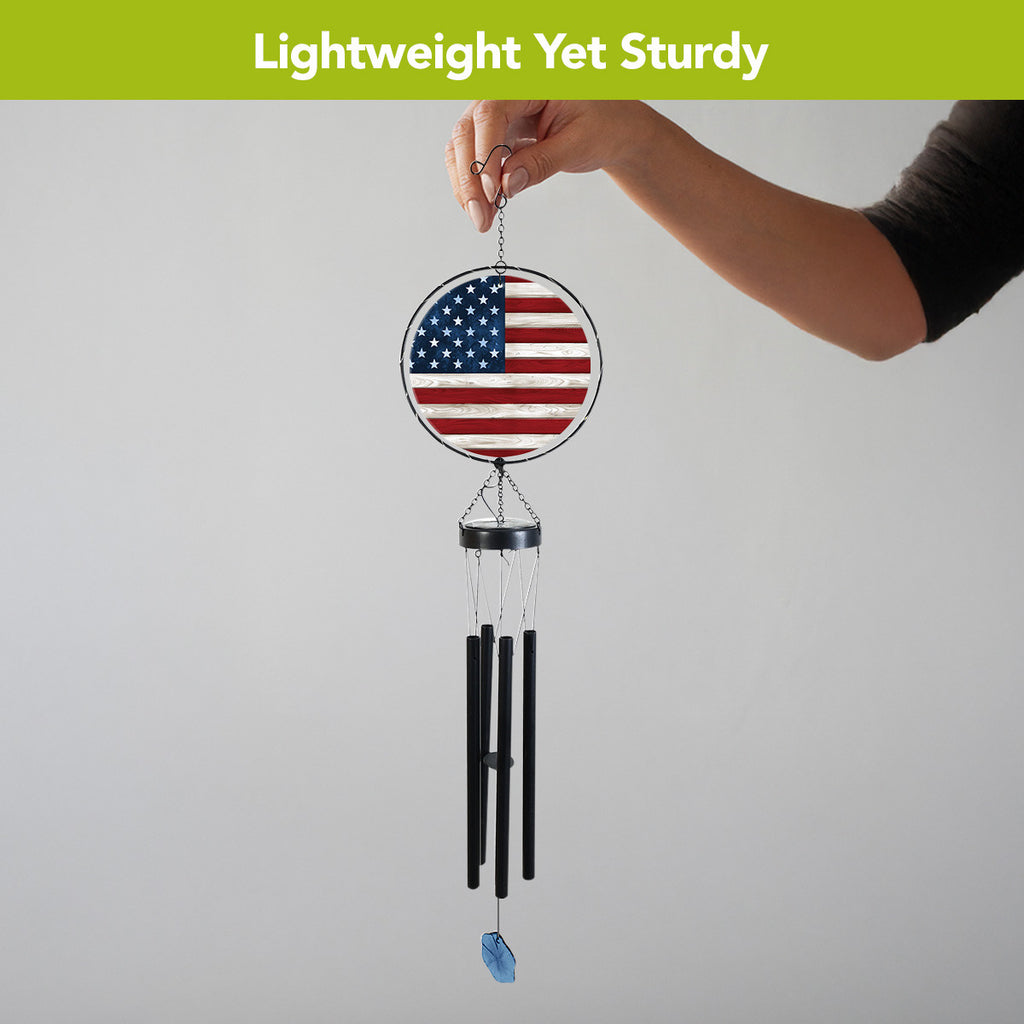 Person holding the American flag wind chime by its hanging hook, showing the full panel, black tubes, and blue wind catcher.