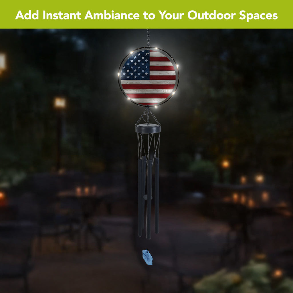 American flag wind chime hanging outdoors at night with LED lights illuminating the round flag panel.