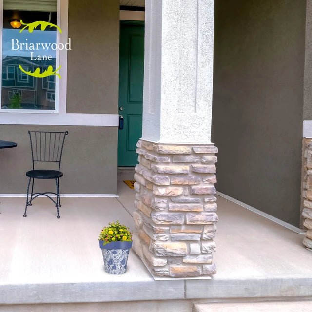 Blue and white floral planter filled with yellow flowers beside a stone column on a front porch.