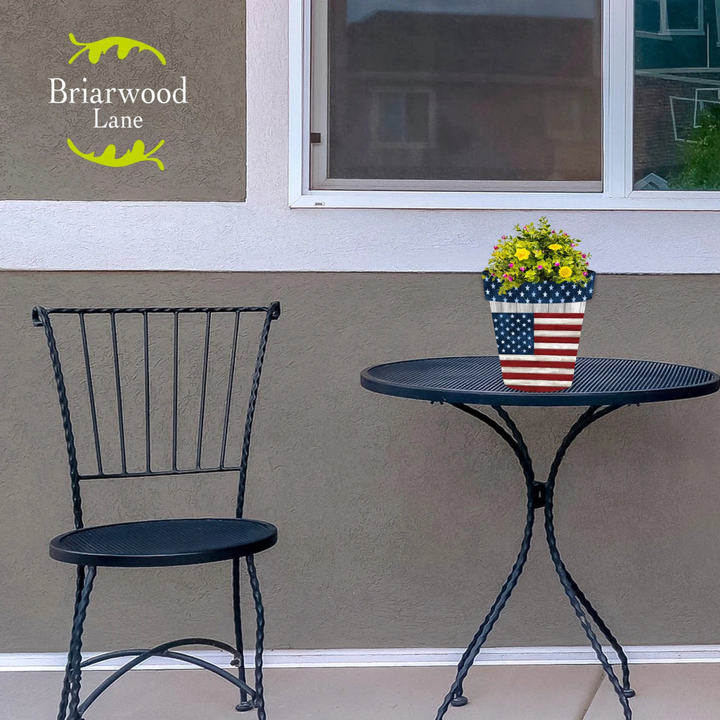 American flag planter filled with yellow and pink flowers on a black metal patio table.