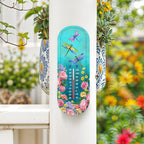 Turquoise dragonfly and floral thermometer mounted on a white porch post beside flowering plants.