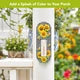 Checkered Sunflowers metal thermometer mounted on a white porch post beside flowering plants.