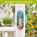 Turquoise hummingbird and floral thermometer mounted on a white porch post beside flowering plants.