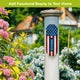 Garden photo: “American flag metal thermometer mounted on a white post beside flowering garden plants.”