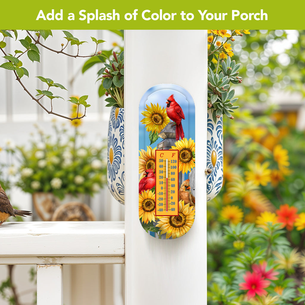 Cardinals and sunflowers metal thermometer mounted on a white porch post beside a blue-and-white hanging planter.