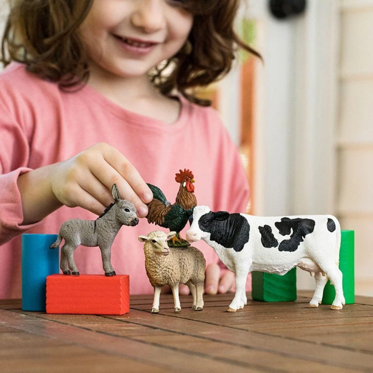 Child playing with Schleich Barnyard Buddies farm animal figures and colorful blocks on a wooden table.