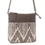 Angled view of Myra Coffee Canvas Crossbody Bag with genuine leather and neutral patterned rug detailing