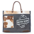 Front view of Myra Dakota Trail Weekender Bag with hair-on hide pocket, dark canvas, leather handles and printed design