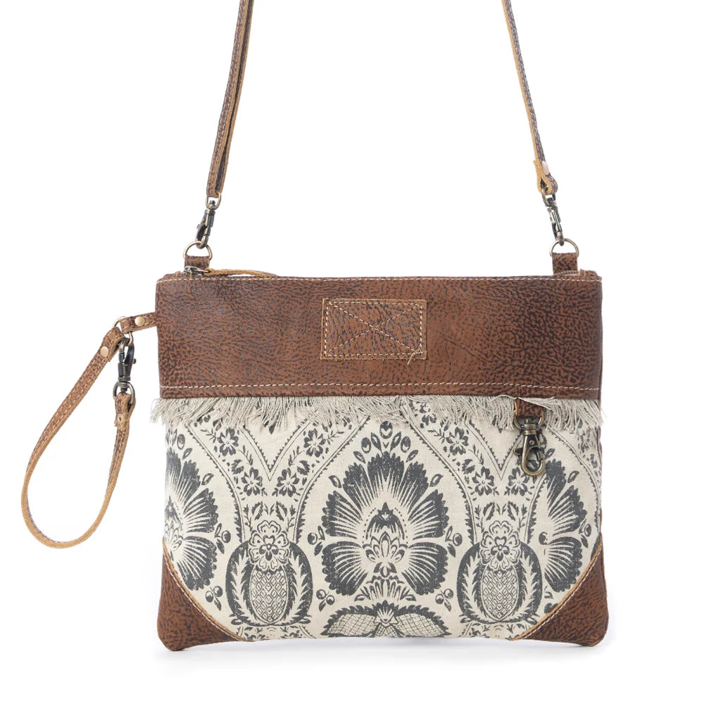 Front view of Myra Floral Flow Crossbody Bag with black floral print, brown leather trim and fringe detail