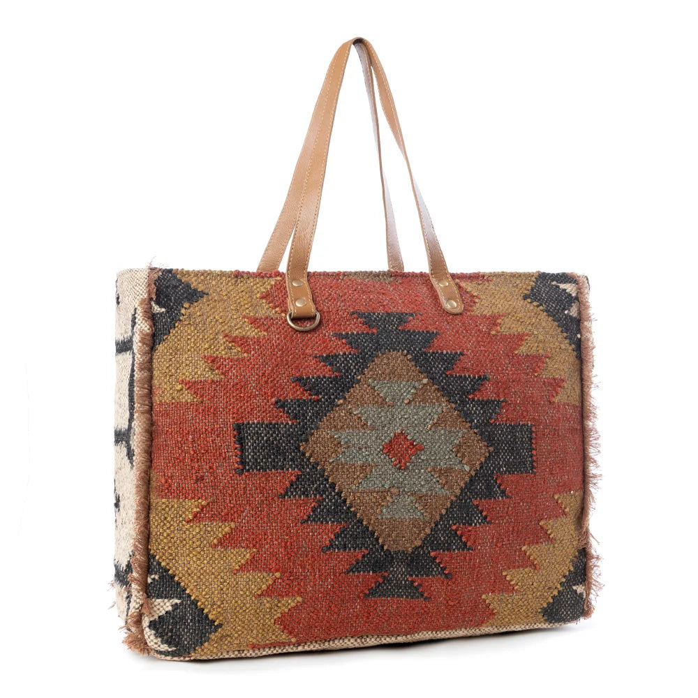 Side view of the Myra Kaliko Hill Canvas Weekender Bag featuring a colorful boho woven pattern and leather shoulder handles.