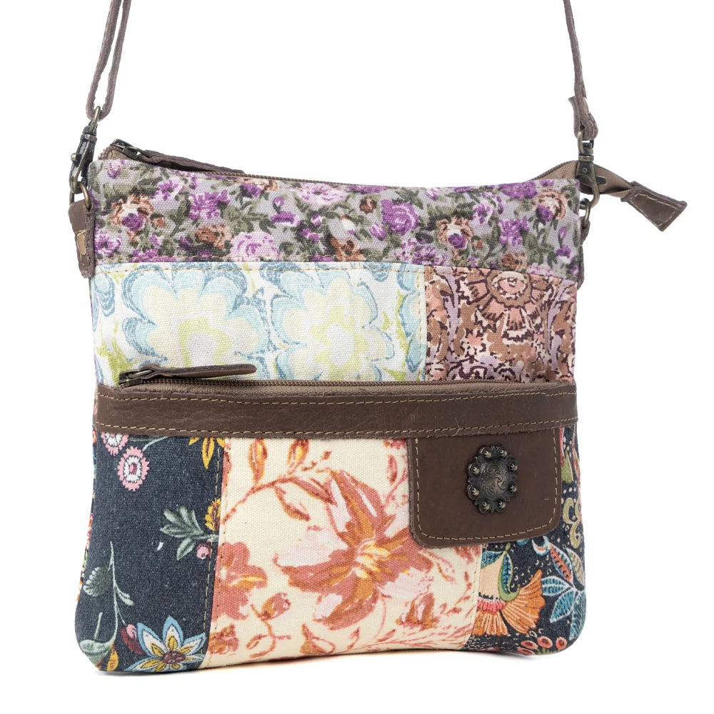 Angled view of Myra La Fleur Patchwork Crossbody Bag with multicolor floral patchwork and brown leather details