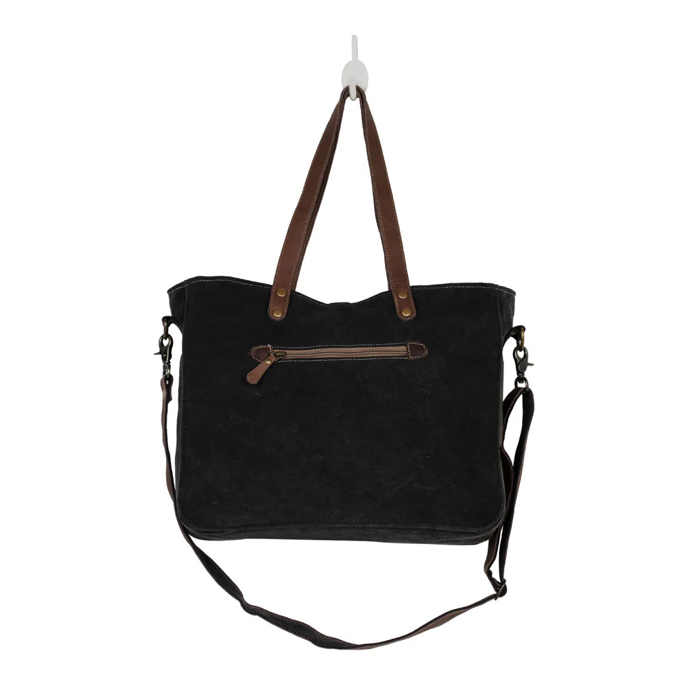 : Back view of Myra Mystique messenger bag with dark upcycled canvas, leather handles and zippered pocket.