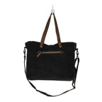 : Back view of Myra Mystique messenger bag with dark upcycled canvas, leather handles and zippered pocket.