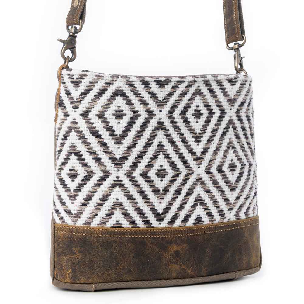Angled view of Myra Precision Crossbody Bag with black and white geometric rug pattern and brown genuine leather trim