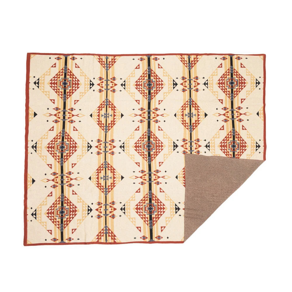 Cream throw blanket with rust, gold, and black geometric medallions and a folded corner showing the tan reverse.