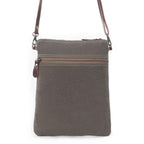 Back of Myra Ruggy crossbody bag showing gray canvas, a zippered pocket, and brown leather strap attachments