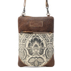 Myra Soul Searcher crossbody bag with black floral print on cream canvas, brown leather trim, and front zip pocket.