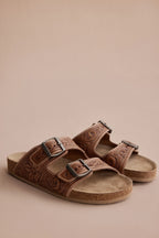 Pair of Myra Darla Trail caramel leather sandals with floral tooling and double-buckle straps on a tan background.