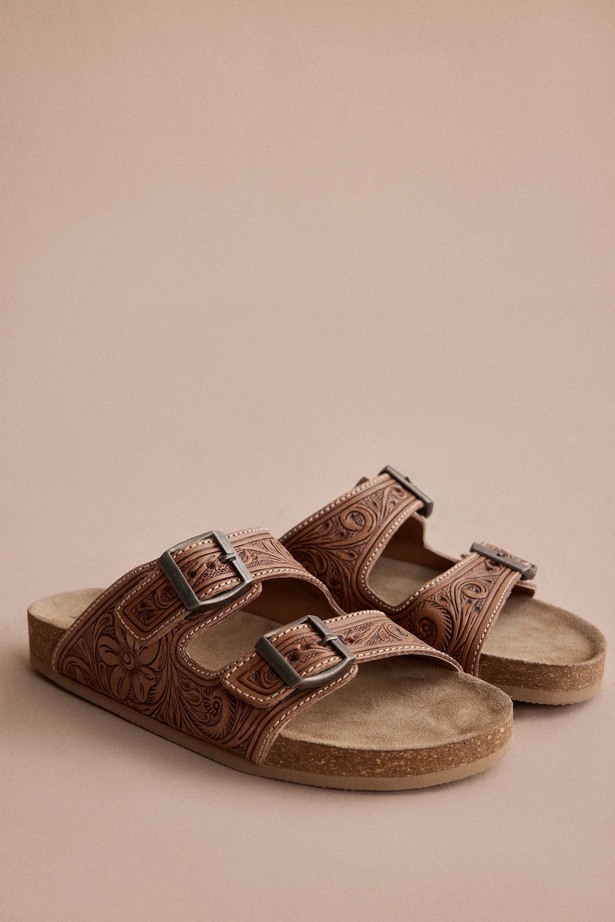 Pair of Myra Darla Trail caramel leather sandals with floral tooling and double-buckle straps on a tan background.